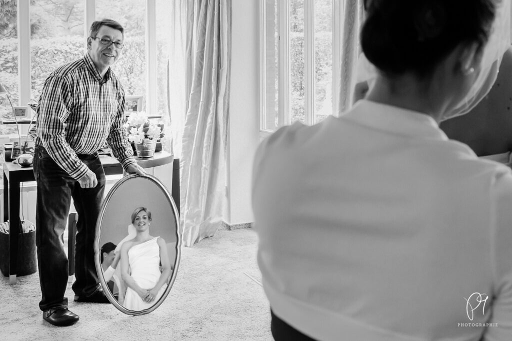 Der Brautvater hält einen Spiegel, damit sich die Braut betrachten kann.