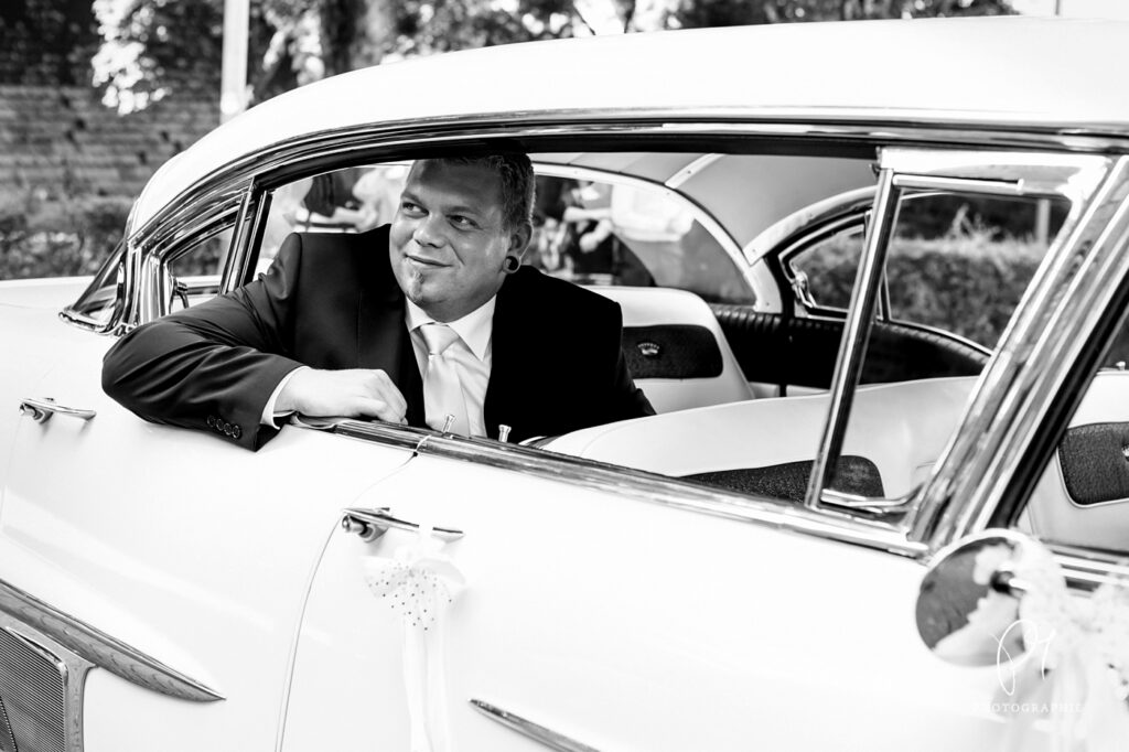 Ein Bräutigam schaut aus dem Hochzeitsauto heraus. Dieses schwarzweiss Foto stammt aus einer Hochzeitsreportage aus Haan. Aufgonommen wurde dieses Hochzeitsfoto mit der Canon 5D und mit Lightroom bearbeitet.