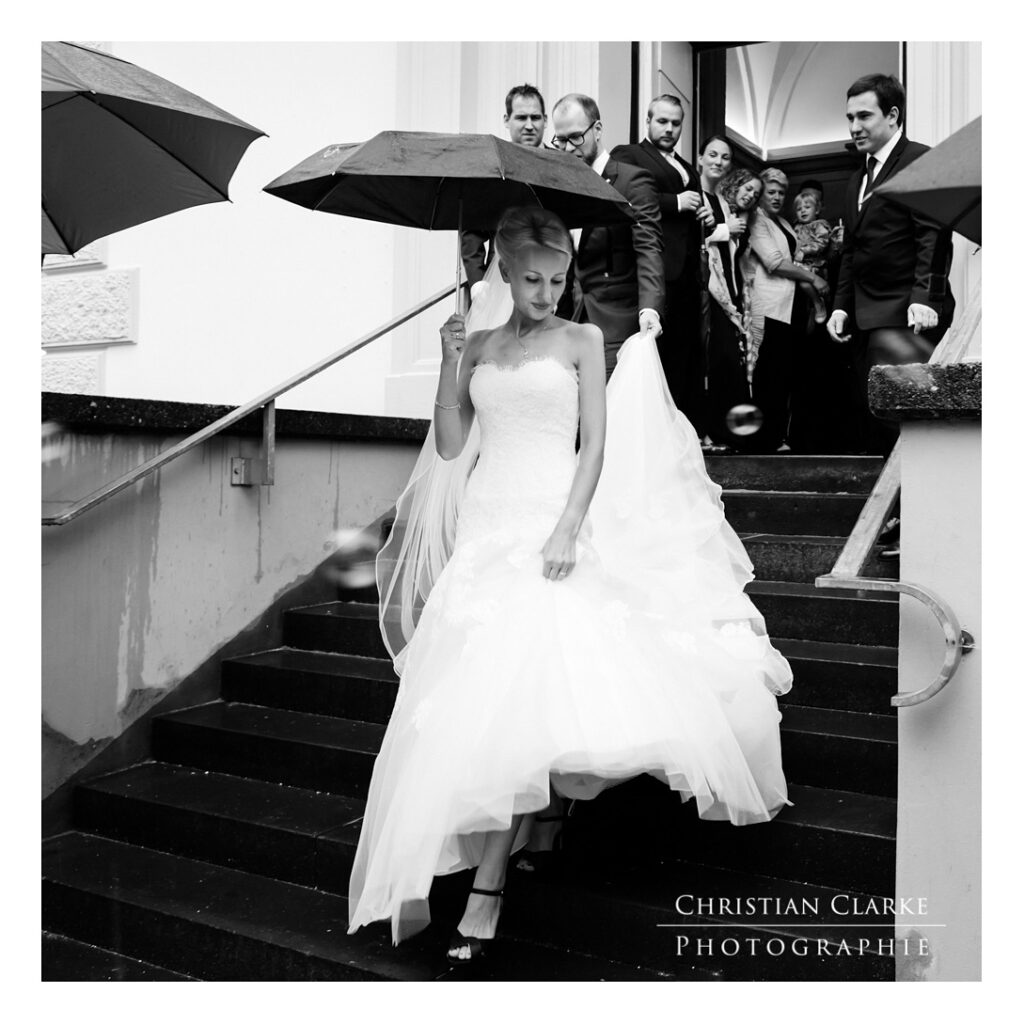 Eine Braut mit verlässt nach einer Trauung die evangelische Kirche in Solingen Wald. Da es regnet, hält sie einen Regenschirm. Aufgenommen wurde dieses Hochzeitsfoto mit der Canon 5D Mark IV.