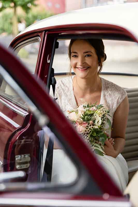 Die Braut sitzt im Hochzeitsauto und hält ihren Brautstrauss.