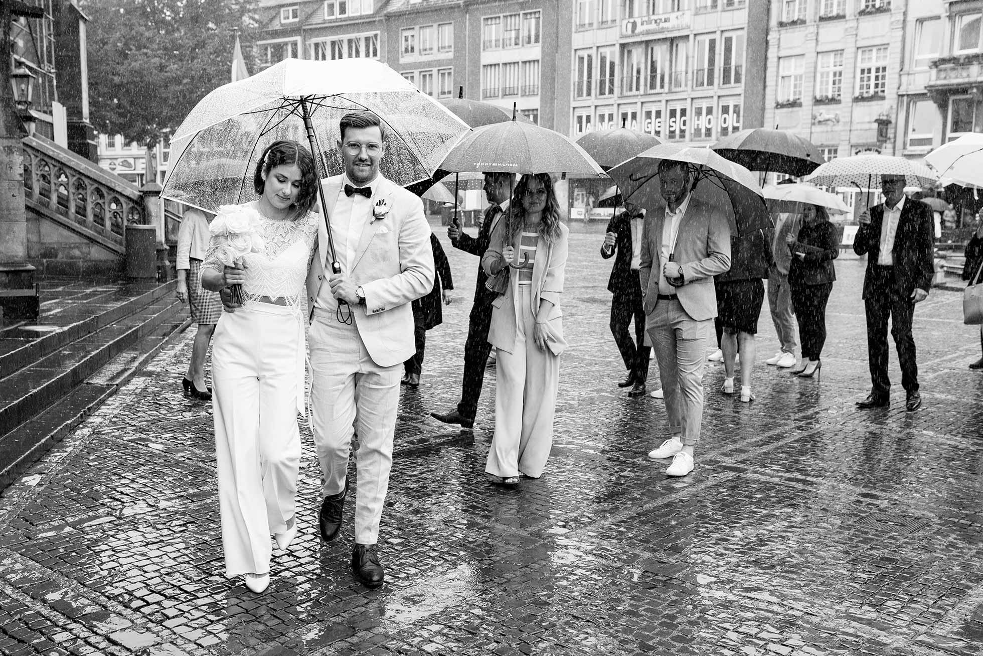 Das Brautpaar und ihre Gäste gehen zur Trauung ins Rathaus Aachen. Dieses Hochzeitsfoto wurde im Regen aufgenommen